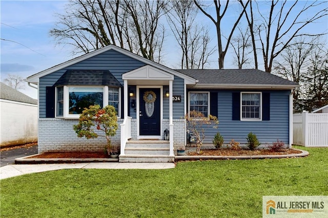 view of front of house with brick siding, a shingled roof, a front yard, and fence