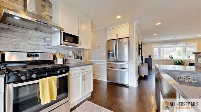 kitchen with ornamental molding, white cabinetry, appliances with stainless steel finishes, wall chimney range hood, and decorative backsplash