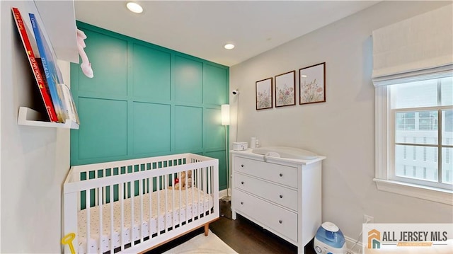 bedroom featuring recessed lighting, a nursery area, and dark wood finished floors