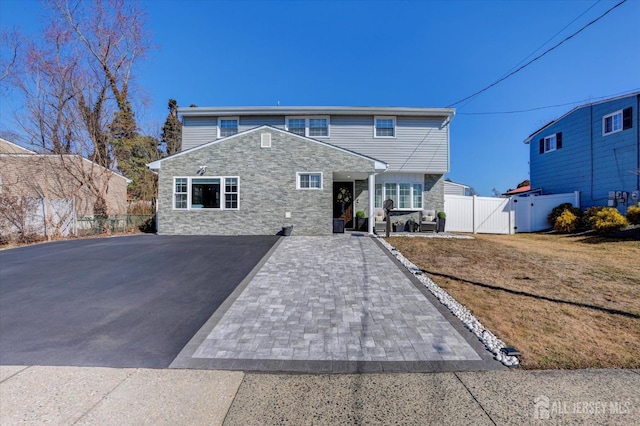 view of front facade featuring driveway, stone siding, a gate, fence, and a front lawn