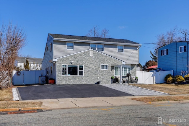 view of front facade with stone siding, a gate, and aphalt driveway