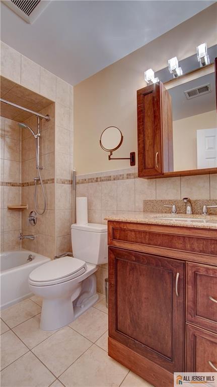 1141 Schmidt Ln, North Brunswick, NJ 08902 - bathroom with tile walls, toilet, tile patterned floors, vanity, and bathing tub / shower combination