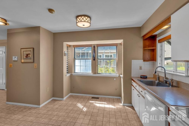 kitchen featuring white dishwasher, a sink, a wealth of natural light, and white cabinetry