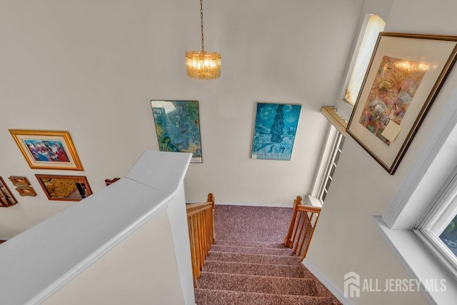 stairway featuring baseboards, a chandelier, and carpet