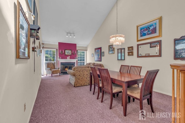 carpeted dining area with baseboards, a warm lit fireplace, a chandelier, and high vaulted ceiling