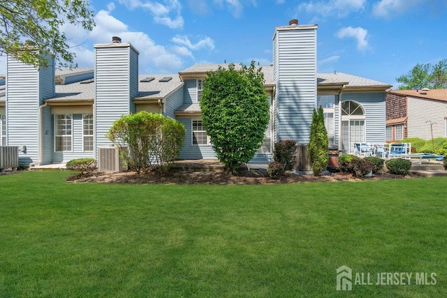 rear view of property with a lawn, a shingled roof, a chimney, and central AC unit