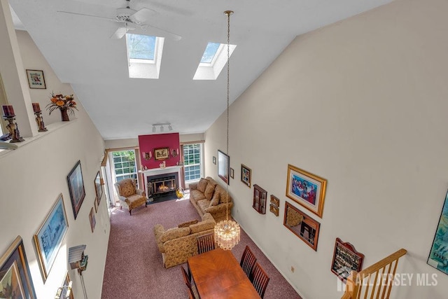 carpeted living area with a fireplace with flush hearth, high vaulted ceiling, a skylight, and ceiling fan