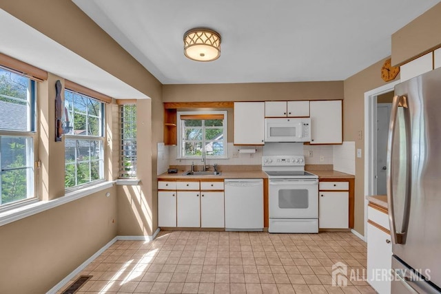 kitchen with visible vents, a sink, light countertops, baseboards, and white appliances