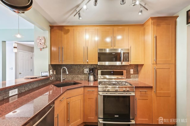 kitchen featuring stainless steel appliances, sink, decorative light fixtures, dark stone countertops, and track lighting