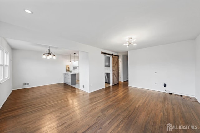 unfurnished living room with a barn door, dark hardwood / wood-style floors, and an inviting chandelier