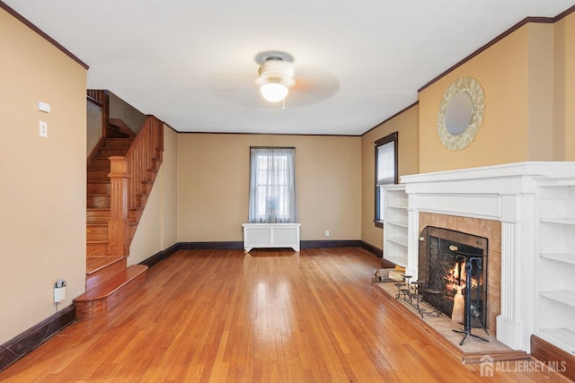 unfurnished living room with radiator, ceiling fan, ornamental molding, a fireplace, and wood-type flooring