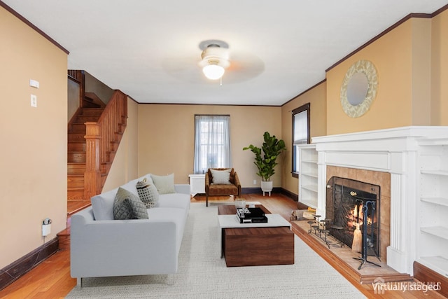 living room with a tile fireplace, crown molding, ceiling fan, and light hardwood / wood-style floors