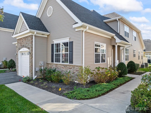 view of front of home featuring an attached garage, stone siding, driveway, and roof with shingles