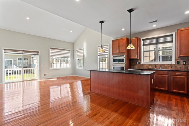 kitchen featuring dark wood-type flooring, tasteful backsplash, dark stone countertops, a kitchen island, and pendant lighting