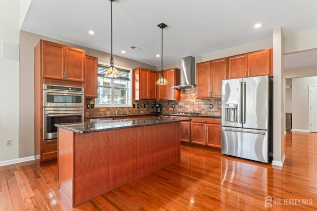 kitchen featuring hanging light fixtures, a center island, wall chimney exhaust hood, and appliances with stainless steel finishes