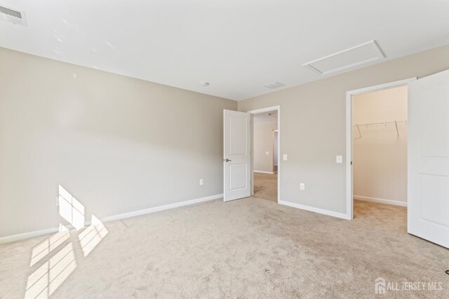 unfurnished bedroom featuring a walk in closet, light colored carpet, and a closet