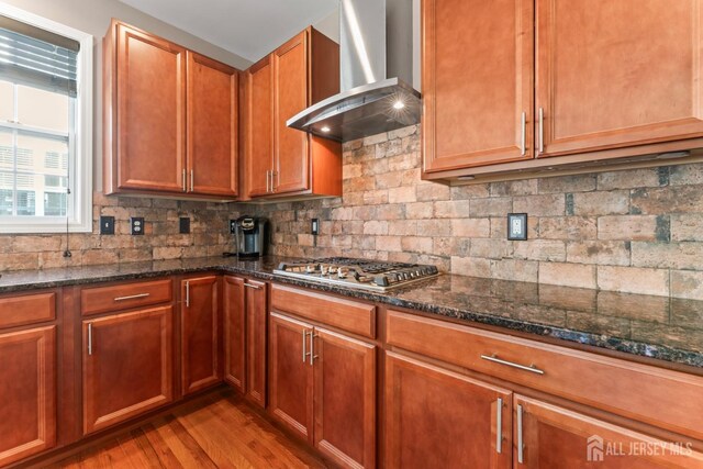 kitchen with dark stone countertops, stainless steel gas stovetop, and wall chimney exhaust hood