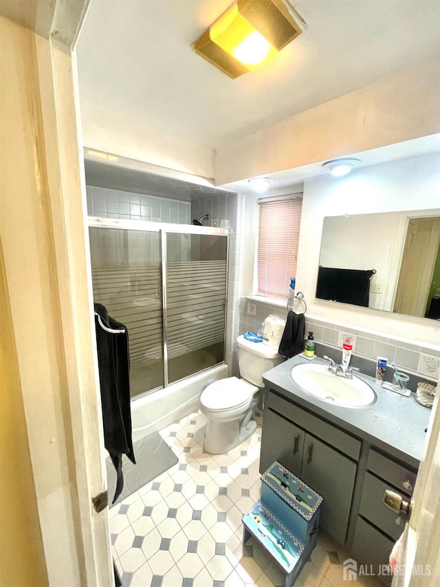 full bathroom featuring vanity, backsplash, toilet, and bath / shower combo with glass door