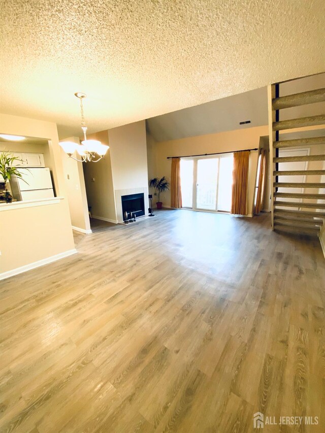 unfurnished living room featuring hardwood / wood-style flooring, a textured ceiling, and an inviting chandelier