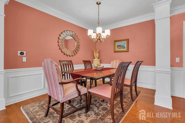 dining area featuring crown molding, wainscoting, a chandelier, light wood-type flooring, and ornate columns