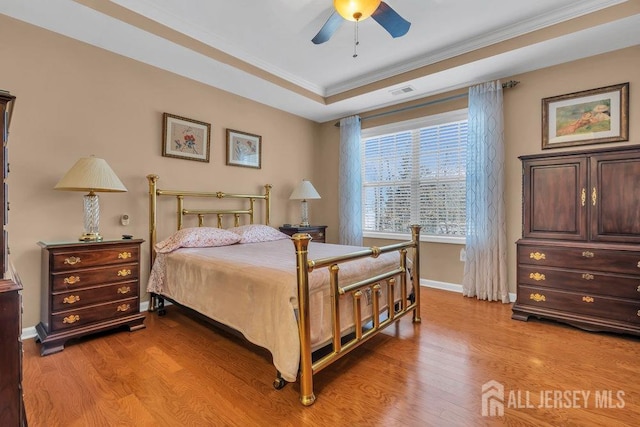 bedroom with light wood-style flooring, baseboards, a raised ceiling, and ornamental molding