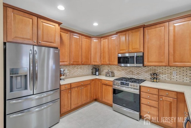 kitchen featuring brown cabinetry, tasteful backsplash, stainless steel appliances, and light countertops