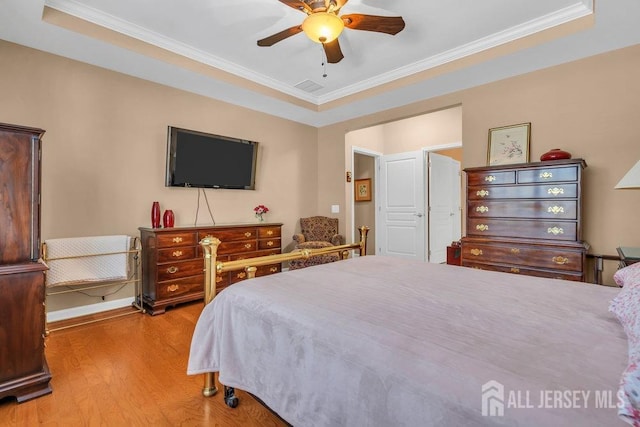 bedroom featuring a ceiling fan, ornamental molding, a raised ceiling, and wood finished floors