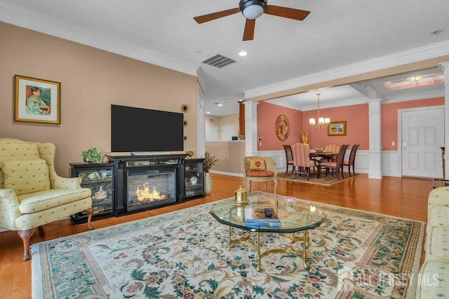 living area with wood finished floors, decorative columns, visible vents, and crown molding