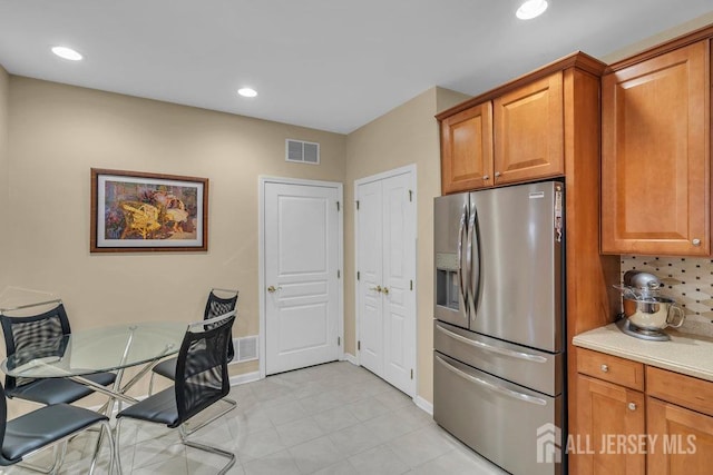 kitchen featuring brown cabinets, stainless steel fridge, and visible vents