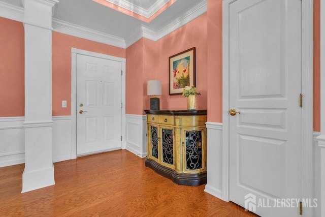 entryway with a wainscoted wall, wood finished floors, a decorative wall, and ornamental molding