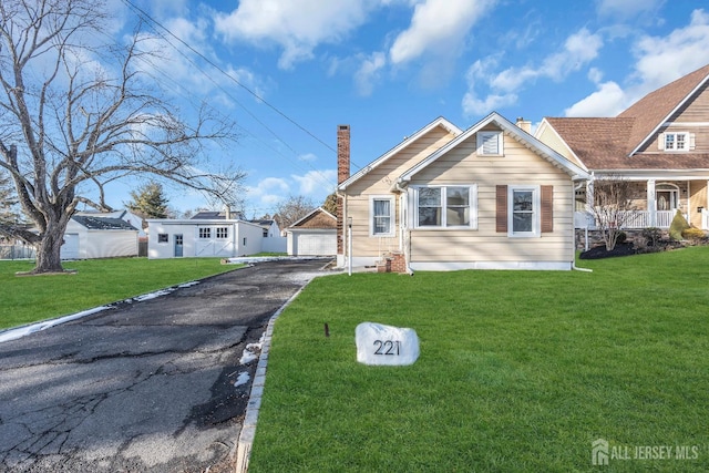 view of front of house with an outbuilding, a front lawn, a detached garage, and a chimney