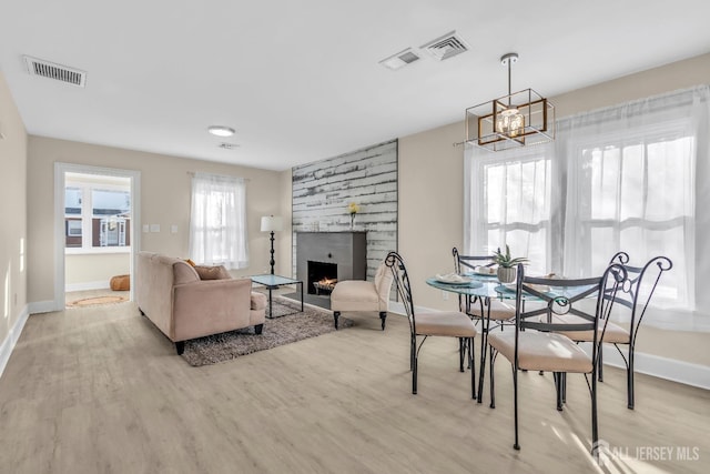 dining area featuring visible vents, a large fireplace, baseboards, a chandelier, and wood finished floors