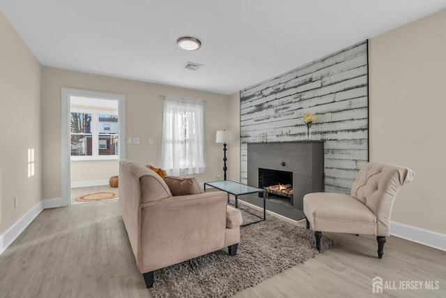 living area with wood finished floors, a fireplace, visible vents, and baseboards