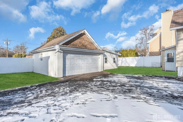 snow covered garage with a lawn and fence