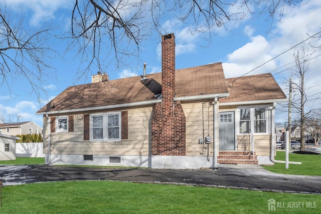 view of front of property featuring entry steps, a front lawn, a shingled roof, and a chimney