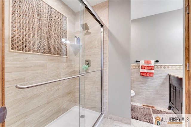 bathroom featuring vanity, toilet, a shower with shower door, and tile walls