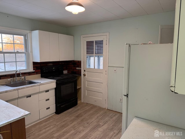 kitchen featuring sink, light wood-type flooring, black range with electric cooktop, white fridge, and white cabinets