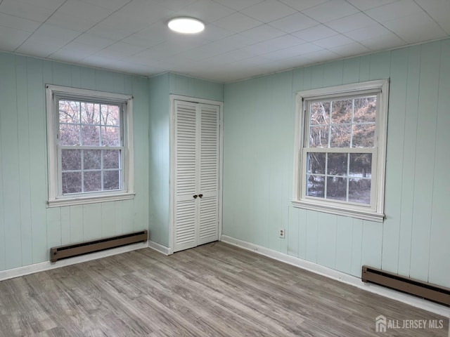 unfurnished bedroom with light wood-style flooring, baseboards, baseboard heating, and a closet