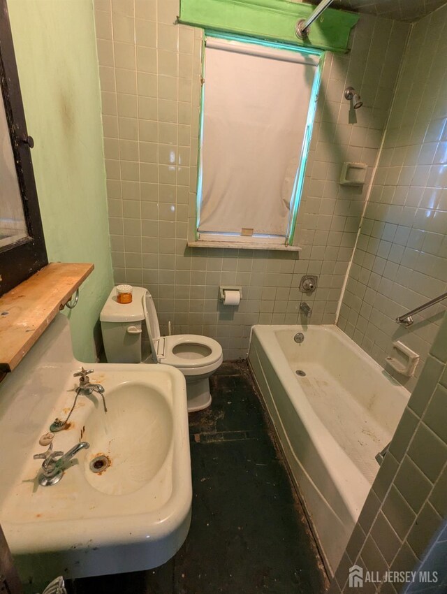 full bathroom featuring toilet, tiled shower / bath combo, sink, and tile walls