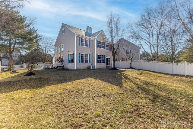 rear view of property featuring a yard, a chimney, and a fenced backyard