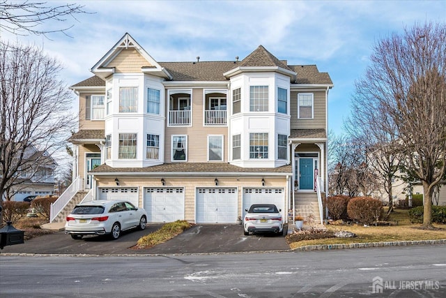 multi unit property featuring driveway, a garage, stairway, and roof with shingles