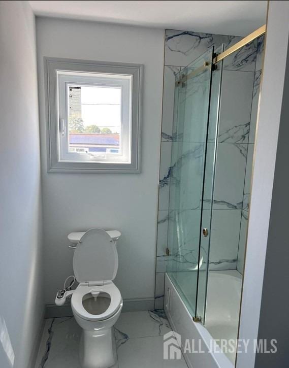 full bathroom with baseboards, toilet, marble finish floor, and bath / shower combo with glass door