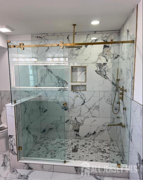 bathroom with a marble finish shower and toilet