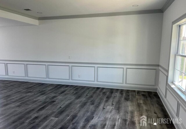 empty room with dark wood-style floors, visible vents, and crown molding