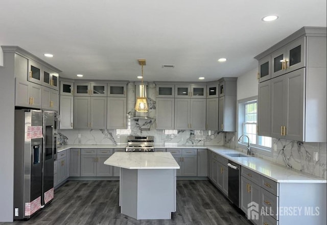 kitchen with gray cabinetry, stainless steel refrigerator with ice dispenser, gas stove, wall chimney exhaust hood, and a sink