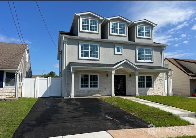 view of front of house with fence, a front yard, stucco siding, stone siding, and driveway