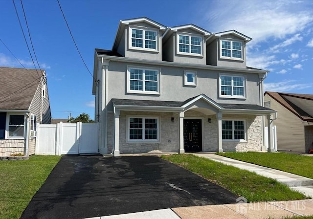 view of front facade featuring stucco siding, a gate, stone siding, fence, and a front yard