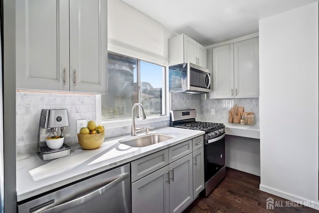 kitchen with sink, gray cabinetry, tasteful backsplash, appliances with stainless steel finishes, and dark hardwood / wood-style flooring