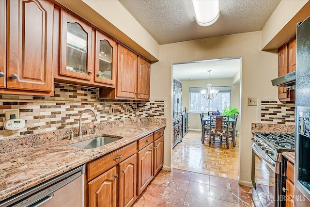 kitchen with glass insert cabinets, light stone countertops, stainless steel appliances, under cabinet range hood, and a sink