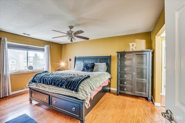 bedroom with a textured ceiling, ceiling fan, light wood-style flooring, visible vents, and baseboards